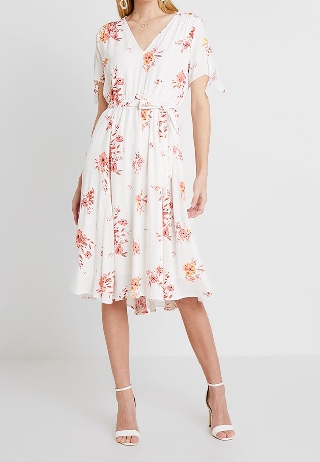 Blommig midiklänning med v-ringning, korta ärmar, vit färg och midjeband. Har rosa och orange blommor mot en ljus bakgrund.