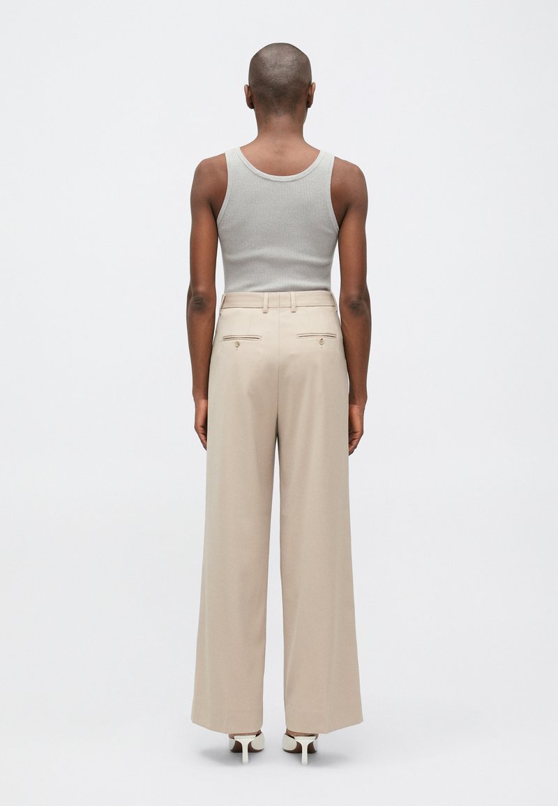 Pantalones de pierna ancha beige con bolsillos traseros, confeccionados en una tela ligera. Combinados con una camiseta sin mangas de canalé gris claro y zapatos de tac�ón altos blancos.
