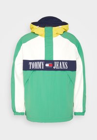 Krāsaini blokota jakas dizains ar zaļiem, baltiem un tumši ziliem paneļiem, ar dzeltenu kapuci. Iekļauts tumši zils saraksts ar "TOMMY JEANS" logo. Strukturēta auduma.