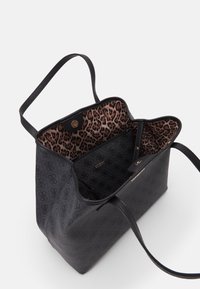 Sac fourre-tout en cuir noir avec un extérieur à motifs, doublure intérieure en imprimé léopard et pochette zippée à l'intérieur, ornée du logo doré "GUESS".