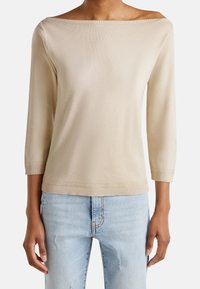 Beige off-the-shoulder topp med trekvartslånga ärmar, ribbad nederkant och en mjuk textur, matchat med ljusblå slitna jeans.