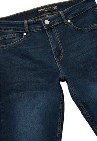 Los pantalones de mezclilla azul oscuro tienen costuras amarillas, un diseño ajustado, un bolsillo frontal, un cierre de botón de metal y una etiqueta en la cintura marcada como W32 L32.