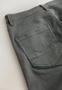 Tumedad hallid denim-püksid sileda tekstuuriga, millel on tagatasku, kus on peen dekoratiivne õmblusdetail ja vöötrupid.