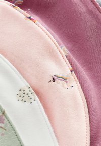 Gros plan d'un tissu rose, mauve, blanc et vert avec des bords cousus et petits motifs de licornes et de cœurs.