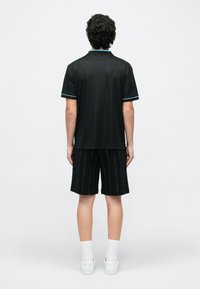 Melna polo krekls ar vertikālām svītrām, gaiši zilas detaļas apkaklē un piedurknēs, kombineēts ar melnām šortiem ar atkārtotu logotipa rakstu.