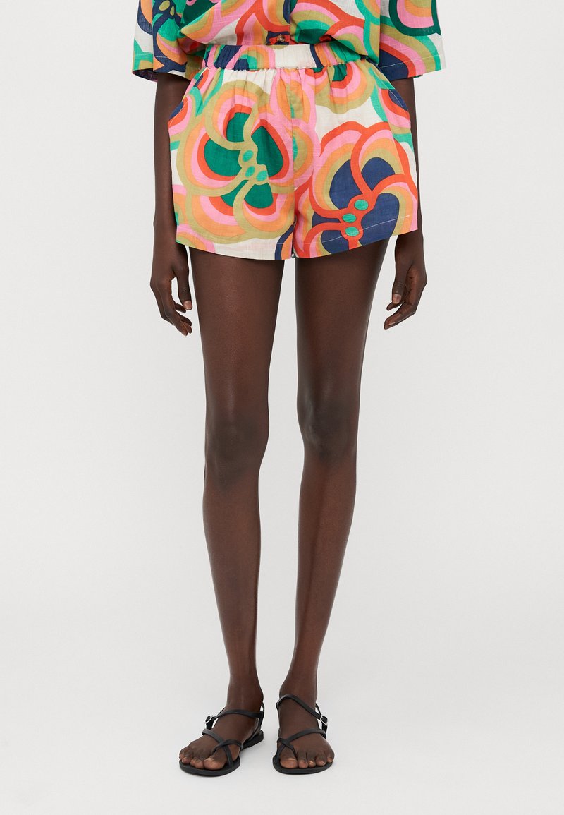 Pantalones cortos de colores con un cinturón elástico, que presentan formas florales curvas en rosa, verde y naranja sobre un fondo claro.