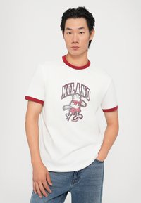 Hvid T-shirt med rød ribbet krave og ærmer, med et grafisk print af en karakter og "MILANO" tekst i et slidt design.