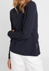 Mörkblå långärmad topp med subtila diagonala vita ränder, lättviktig kvalitet och en avslappnad passform med en sidoknytningsdetalj.