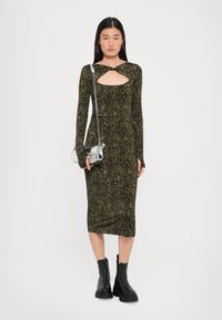 Leopard print long-sleeve dress with a cutout neckline and fitted silhouette, paired with black chunky-heeled ankle boots and a metallic handbag.