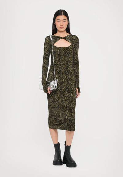 Robe à manches longues en imprimé léopard avec un décolleté découpé et une silhouette ajustée, assortie à des bottines à talons épais noires et un sac à main métallique.