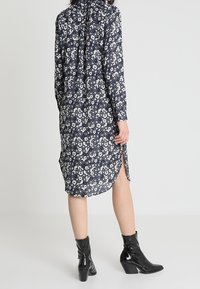 Marinblå blommig klänning med långa ärmar, vitt blommönster, sidoslitsar och krage. Bärs med svarta klackade ankelnaglar.