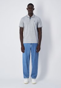 Polo grigio con colletto blu navy, rifiniture bianche e logo ricamato. Abbinato a jeans larghi di un blu chiaro e sneakers bianche.