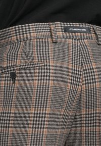 Szürke kockás nadrág, fekete, fehér és narancssárga akcentusokkal; oldalzsebbe fekete gomb részlet is található.