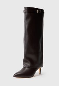 Bota de cuero marrón hasta la rodilla con punta afilada y tacón pequeño, que presenta una parte superior enrollada y un detalle de cinturón cerca de la abertura.