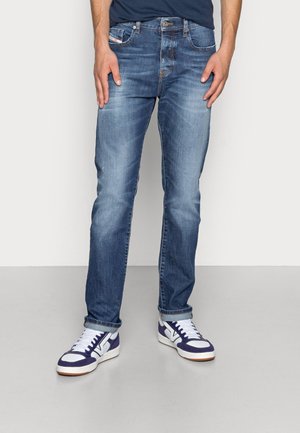 Jeans de mezclilla azul con un diseño de pierna recta, acabado desgastado y estilo clásico de cinco bolsillos. Combinados con zapatillas blancas y marino.