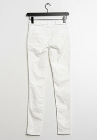 Jeans ajustados de algodón blanco colgados de un gancho negro. Presenta cinco bolsillos y una textura lisa, sin desgastes.