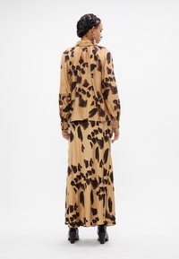 Bruine luipaardprint blouse gecombineerd met een bijpassende lange rok, beide gemaakt van lichtgewicht stof, met een hoge halslijn en pofmouwen.