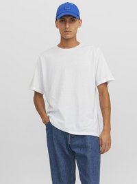 T-shirt en coton blanc avec un col rond, associé à une casquette en coton bleue et un jean en denim bleu ample. Tenue simple et décontractée.