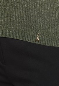 Pull en maille côtelée verte avec un éclat métallique, orné d'une décoration dorée à l'ourlet. Le fond est un tissu noir lisse.