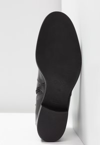 Semelle d'une chaussure en cuir noir avec un talon bas, affichant la marque "Gabor" et la taille "4½", sur un fond blanc.
