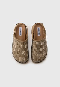 Tan, open-back klompen versierd met zilveren studs en een gestructureerde afwerking, met een gevoerd voetbed en een zwarte rubberen zool.