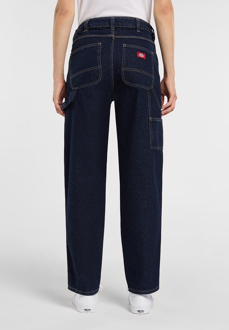 Dark blue denim pants with a relaxed fit, featuring two back pockets and a side pocket. Stitched detailing and a label near the waistband.