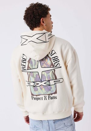 Sudadera con capucha color crema con un gráfico floral en la parte trasera, que presenta texto negro en negrita y un diseño estampado. Detalles de capucha y puños acanalados.