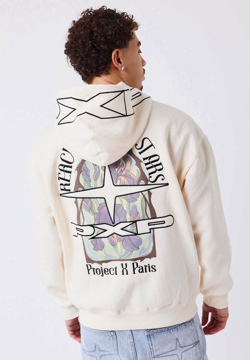 Sweat à capuche couleur crème avec un motif floral au dos, comportant un texte noir audacieux et un design à motifs. Capuche et poignets côtelés en détail.