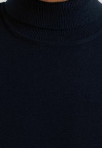 Mörkblå turtleneck-tröja med ribbad textur och en figurformad design. Mjukt material som betonar värme och täckning.