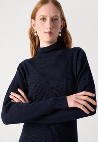 Suéter de cuello alto acanalado en color navy, con patrones verticales y diagonales, mangas largas y un diseño ajustado.