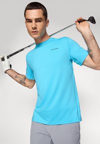 Himmelblaues Golfshirt mit kurzen Ärmeln und Rundhalsausschnitt, versehen mit dem Calvin Klein Logo. Glatte Stofftextur mit einem lässigen Schnitt.