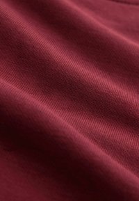 Bordeaux katoenen stof met een gladde textuur en ribbelpatroon, met zachte, golfachtige plooien en een subtiele glans.