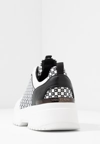 Baskets en noir et blanc avec un motif à damier, un talon rembourré et une semelle blanche élégante avec un logo sur le côté.
