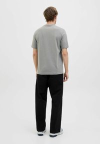 Light gray short-sleeve t-shirt with a round neckline, paired with loose-fitting black pants and gray sneakers, viewed from the back.