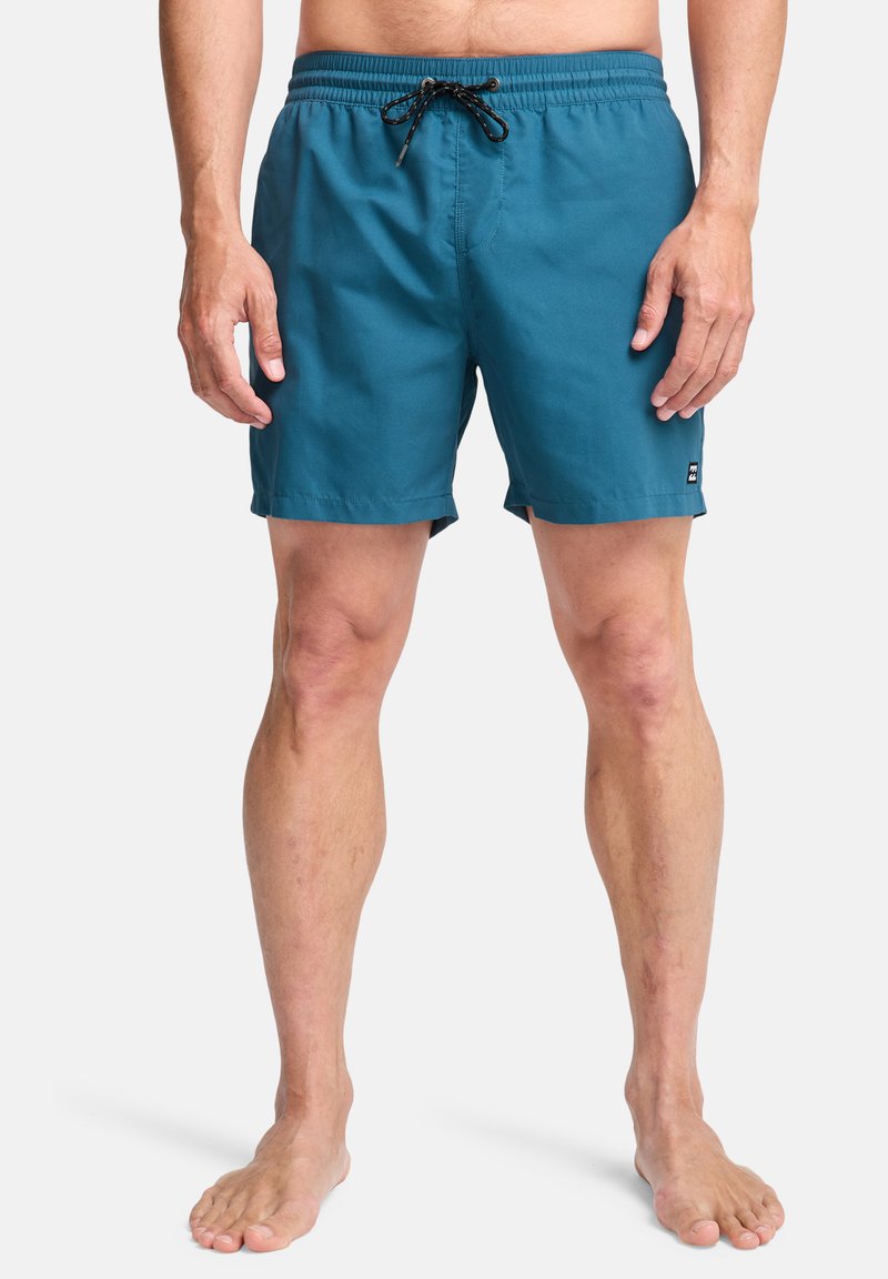 Bañador para hombres en tejido azul verdoso, con una cinturilla elástica y cordón ajustable, bolsillos laterales y un parche con el logo en el dobladillo.