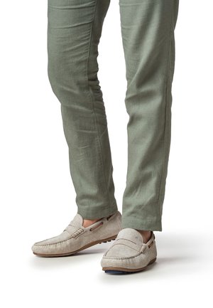 Beige instap loafers met een gestructureerde stof, bruine accenten en rubberen zolen, gecombineerd met slanke olijfgroene broeken.