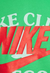 Zelená látka s velkým červeným logem Nike a bílým textem, s texturovaným, prodyšným povrchem a odvážným grafickým designem.