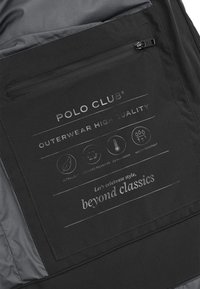 Svart yttertyg med inre etikett som visar "POLO CLUB"-logotypen, skötselikoner och text som anger egenskaper som lätt, varm och vattentålig.