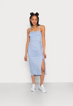 Vestido midi de padrão floral em azul claro, com alças finas ajustáveis, franzido lateral e uma fenda alta, combinado com ténis brancos.
