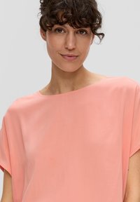 Helles Rosa, lockeres Oberteil mit kurzen Ärmeln und weitem Halsausschnitt. Glatte Textur mit dezentem Glanz. Minimalistisches Design, keine sichtbaren Muster.