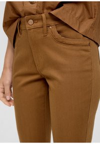 Pantalons en denim marron avec une coupe ajustée, dotés d'une fermeture à bouton, de passants de ceinture et de poches avant. Texture lisse avec une coupe légèrement structurée.