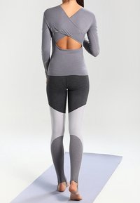 Graues langärmeliges Oberteil mit offenem Rücken und überkreuztem Design, kombiniert mit hoch taillierten Leggings mit Farbblockmuster in Grau und Weiß.