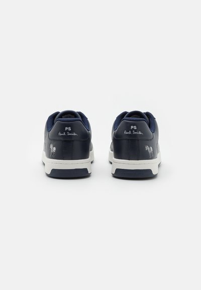 Mörkblå lädersneakers med vita gummisulor, som har ett distinkt zebramönster och logotyp på hälen. Strukturerad nätdetaljering.