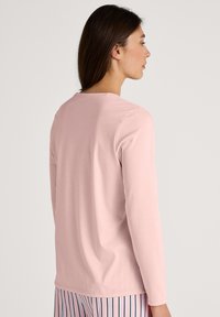 Long-sleeve pink top in soft material, featuring a round neckline and smooth texture. Viewed from the back, paired with striped pajama bottoms.
