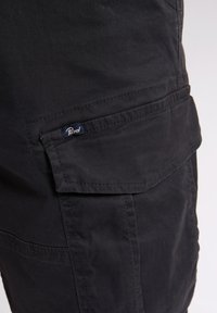 Sorte cargo shorts lavet af slidstærkt stof, med flere lommer og et vævet mærke på siden. Glat tekstur med forstærkede sømme.