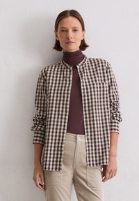 Brown and cream checked shirt with a mandarin collar, button closure, and single chest pocket, worn over a brown turtleneck.