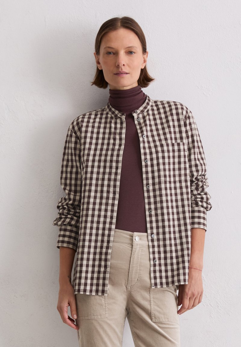 Brown and cream checked shirt with a mandarin collar, button closure, and single chest pocket, worn over a brown turtleneck.