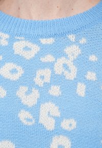 Φωτεινό γαλάζιο πλεκτό πουλόβερ με λευκό μοτίβο λεοπάρ. Στρογγυλή λαιμόκοψη με ριμπ τελείωμα. Μαλακή υφή με μέτριο βάρος.