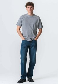 Grå t-shirt med korte ærmer og rund hals, parret med mørkeblå lige ben jeans og sorte sko. Simpelt design, ingen mønstre.