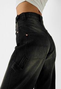 Czarne dżinsowe spodnie cargo z wysokim stanem, z dużymi tylnymi kieszeniami i miedzianymi nitami, prezentujące miękką, teksturowaną powierzchnię.